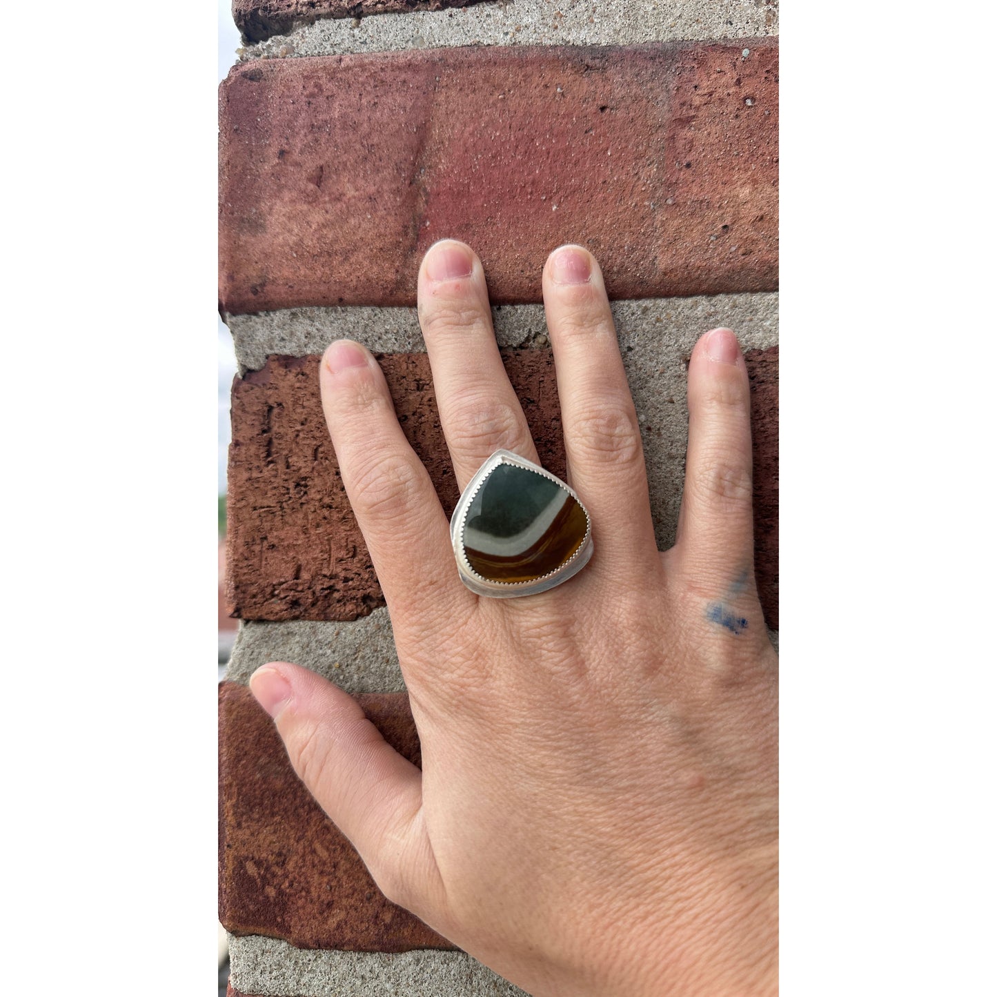 Hand wearing a ring with a stone on a brick surface