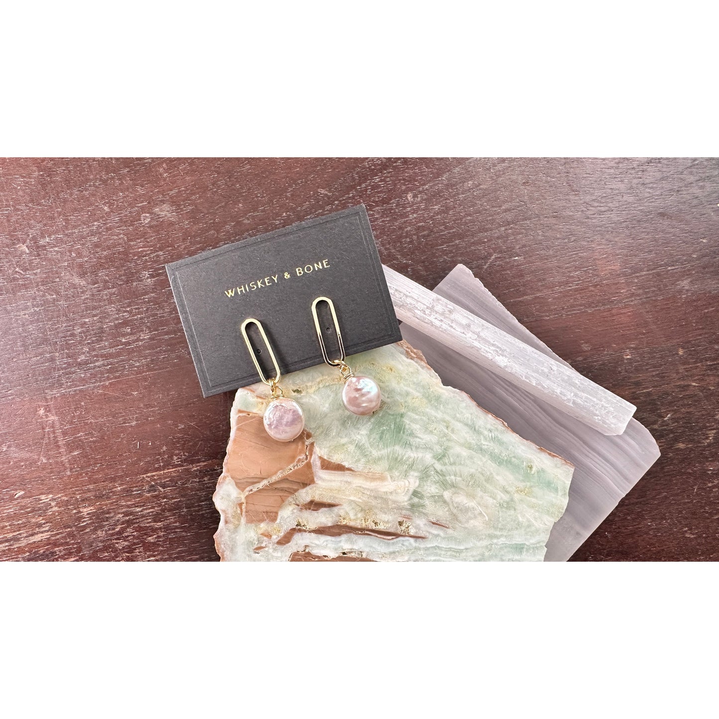 Pair of pearl earrings on a display card with 'Whiskey & Bone' branding, placed on a textured surface.