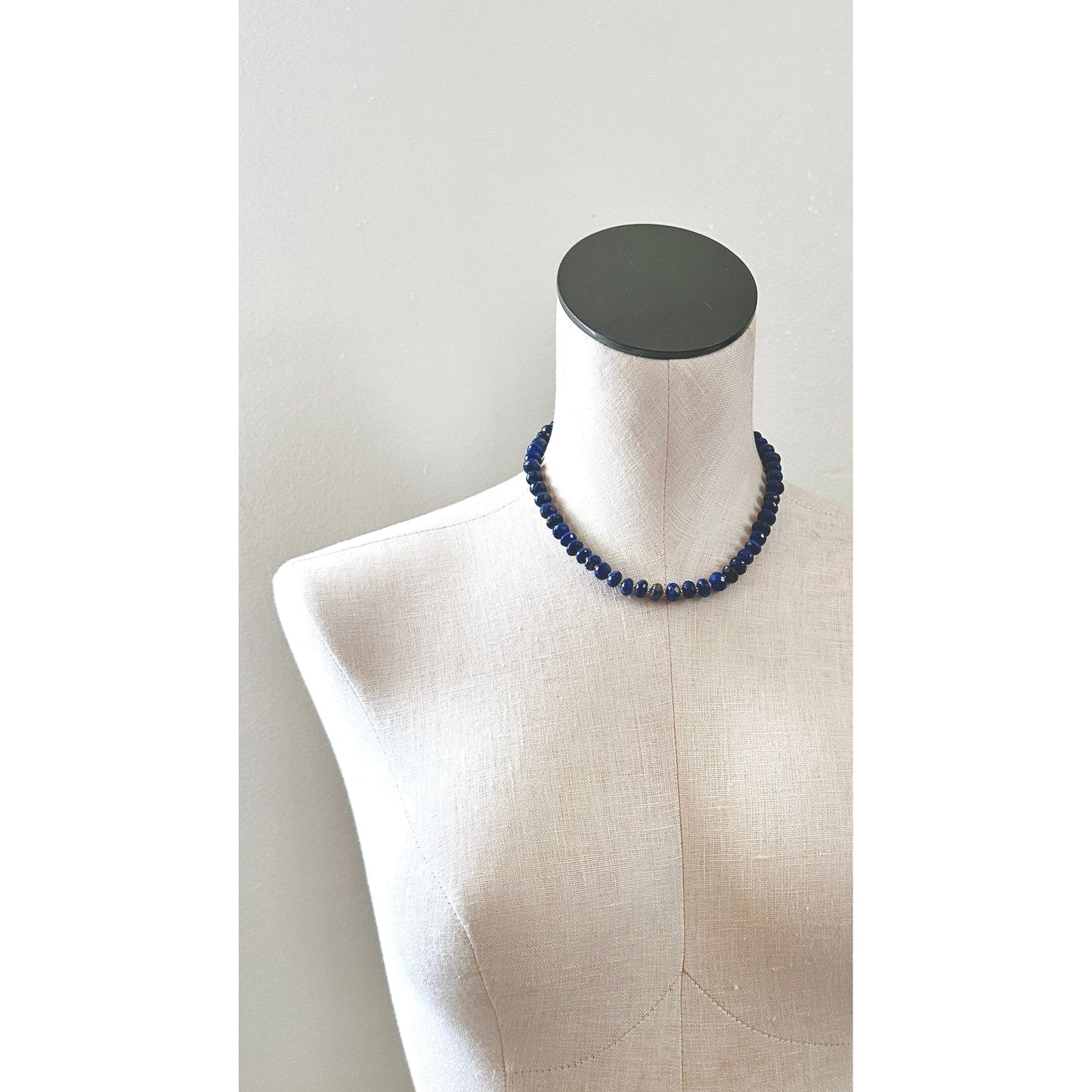 Blue beaded necklace on a mannequin bust against a plain background