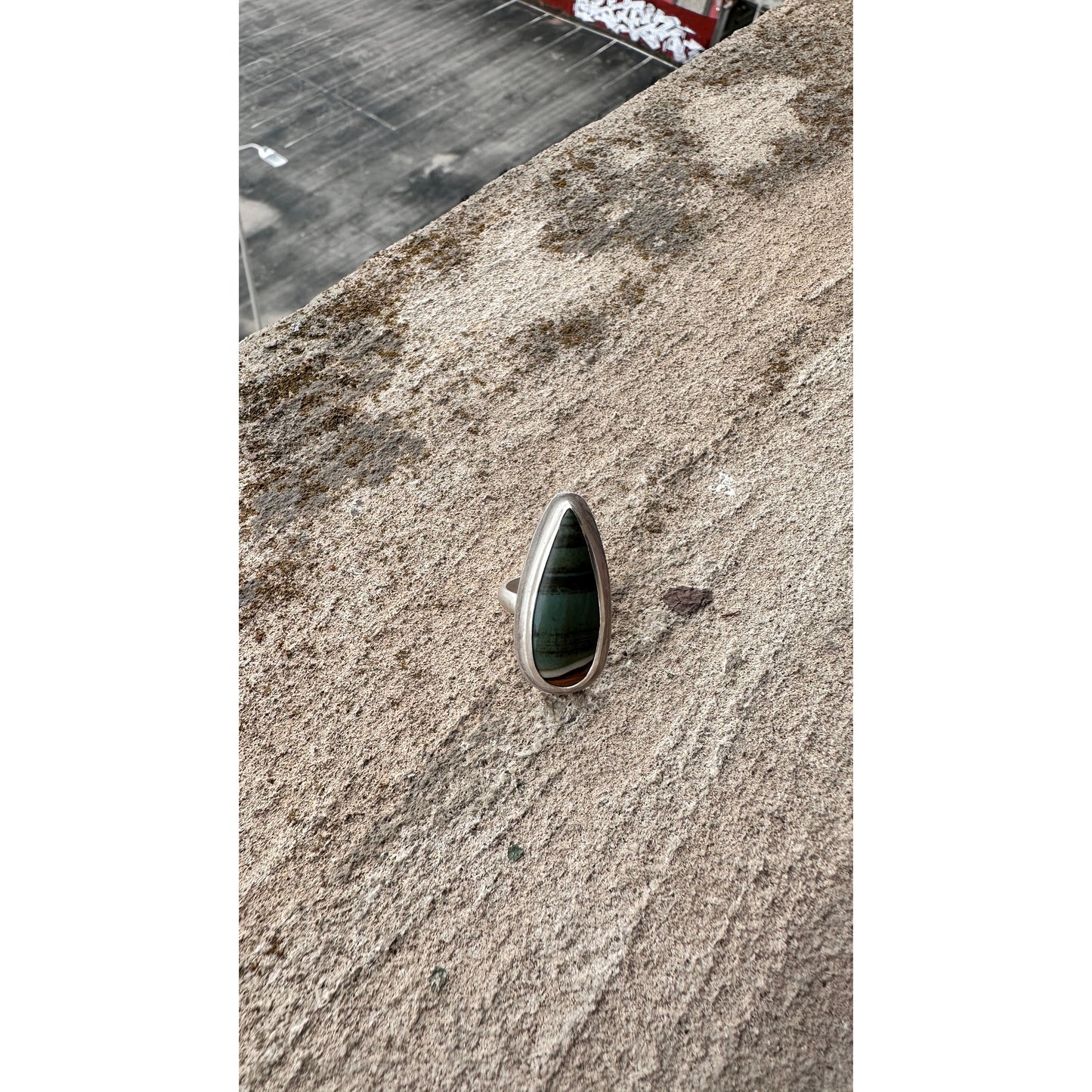 Silver ring with a green stone on a textured surface