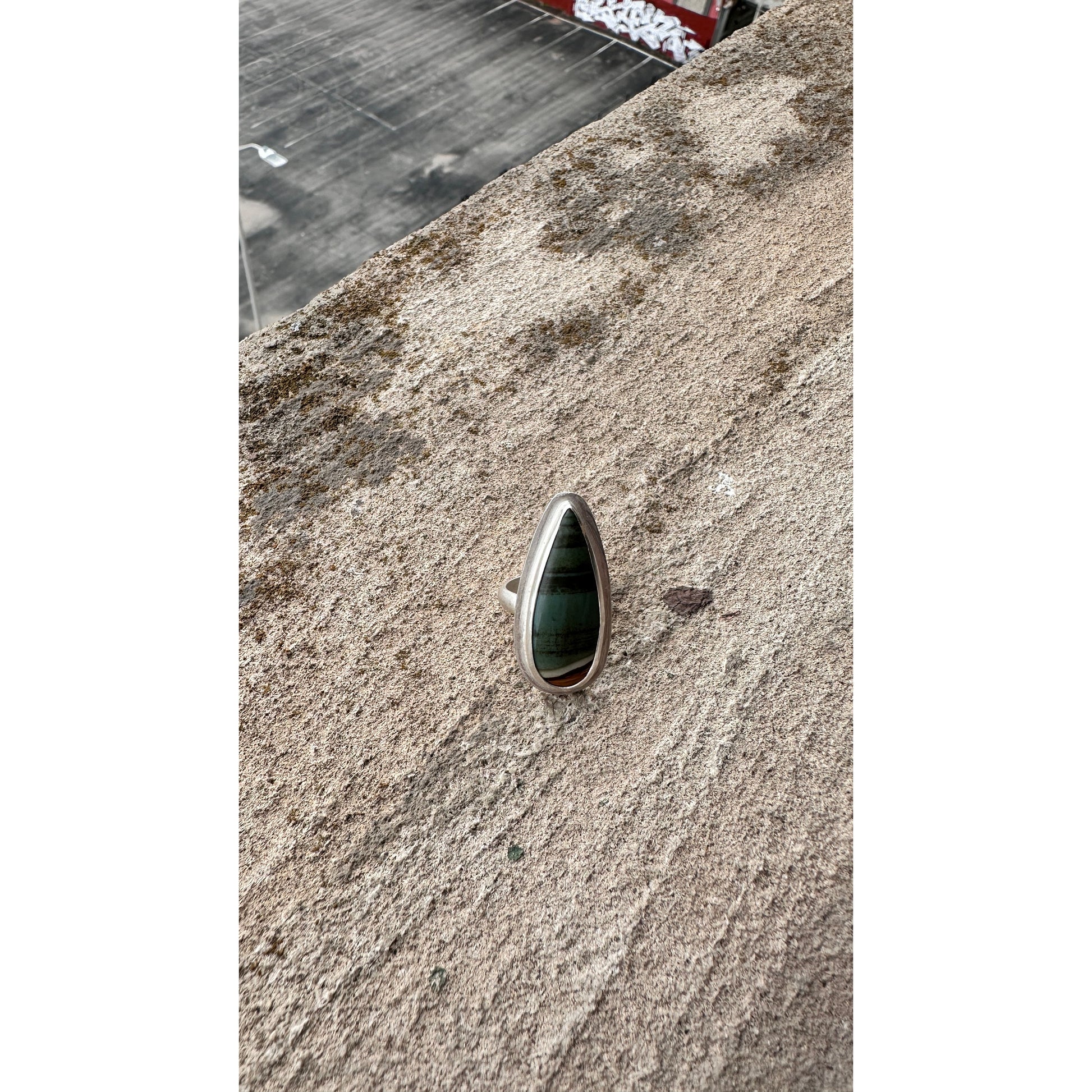 Silver ring with a green stone on a textured surface
