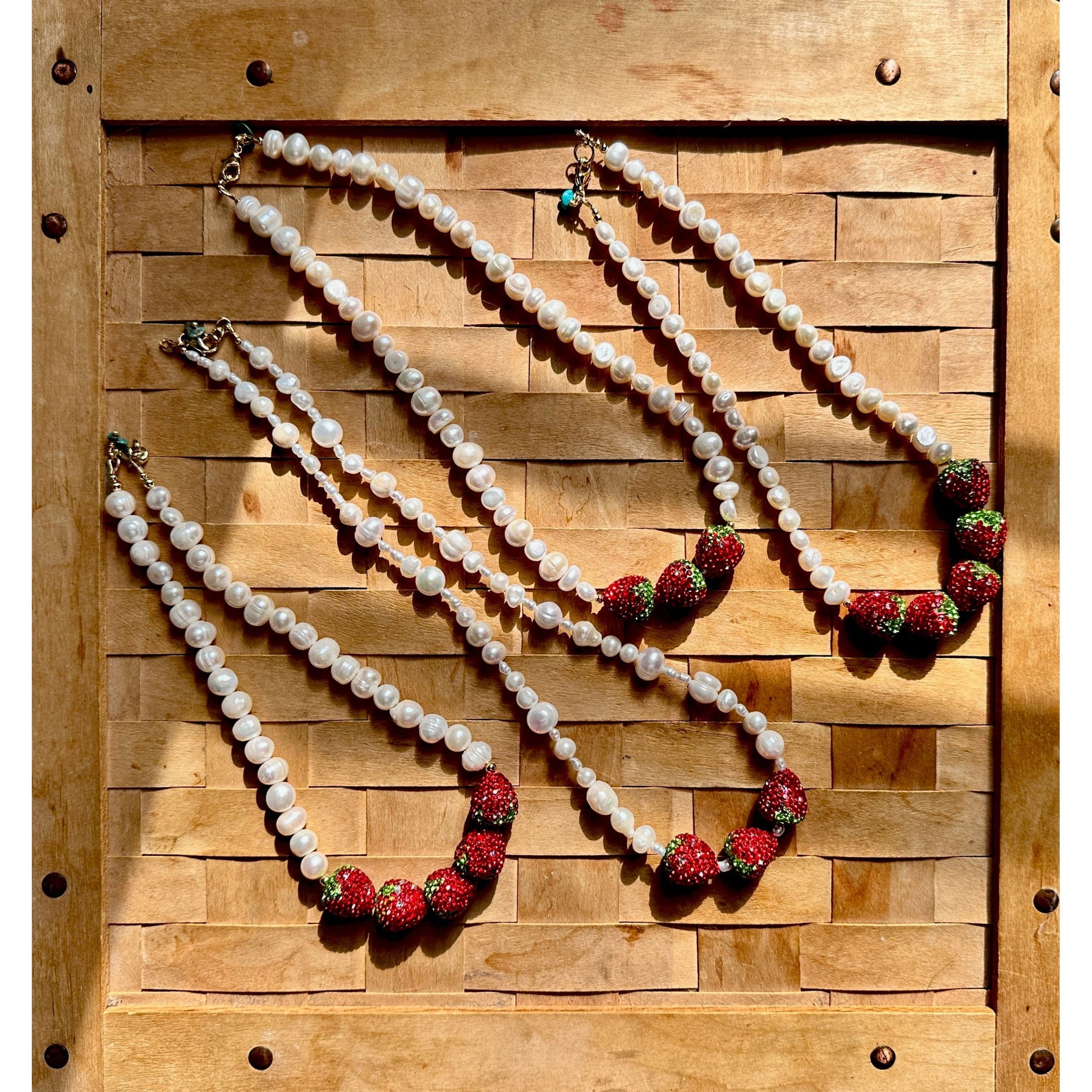 Four pearl necklaces with red and green accents on a wooden background