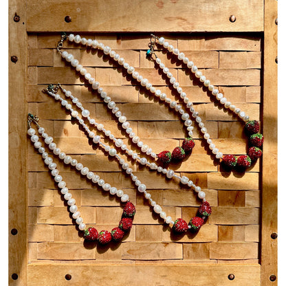 Four pearl necklaces with red and green accents on a wooden background