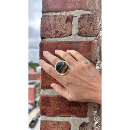 Hand wearing a silver ring with a dark stone on a brick wall background