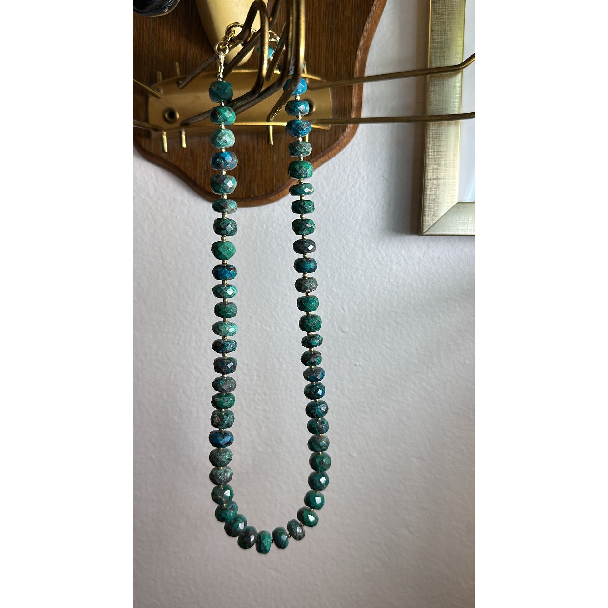 Green beaded necklace hanging on a wooden wall hook against a white background