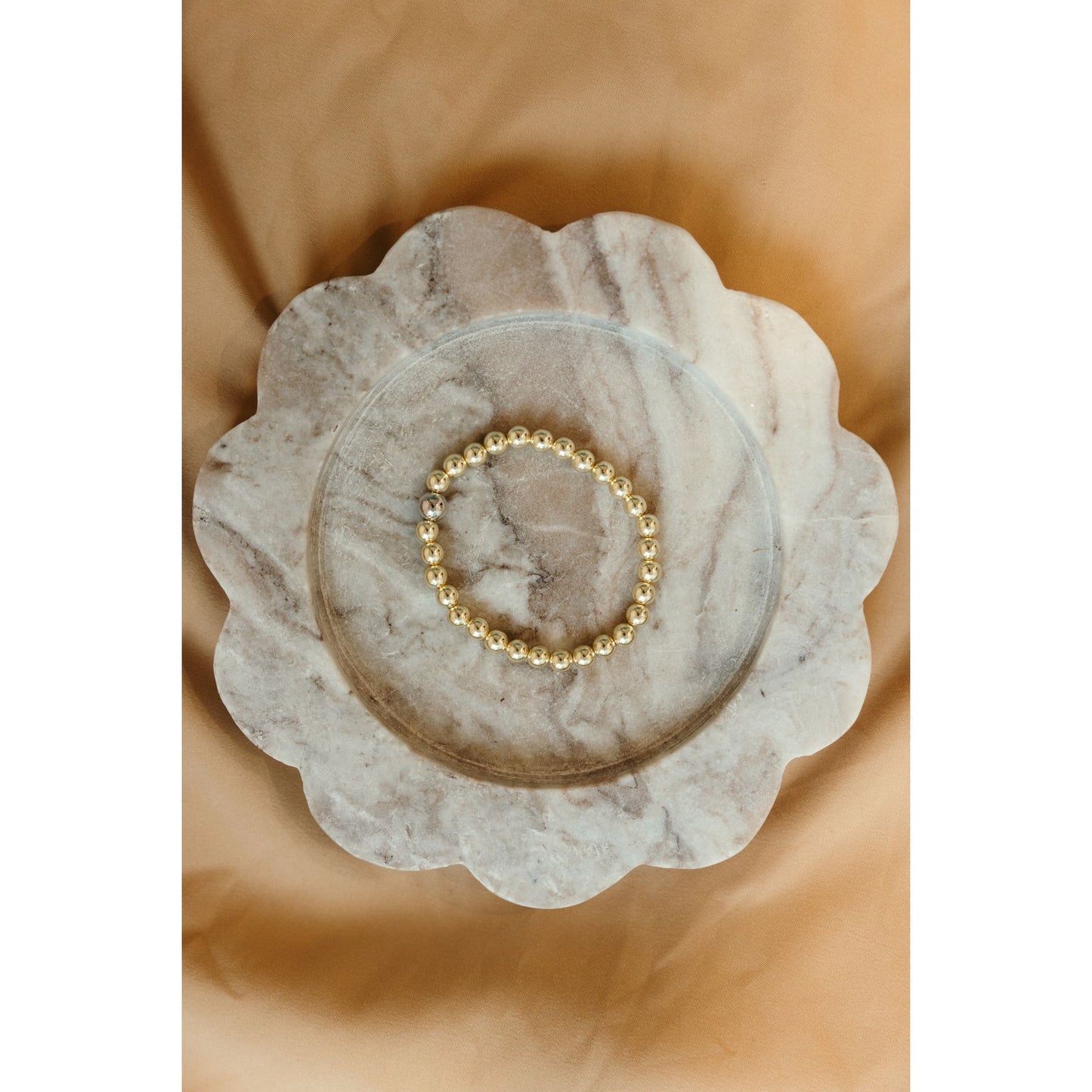 Gold beaded bracelet on a marble dish with a beige background