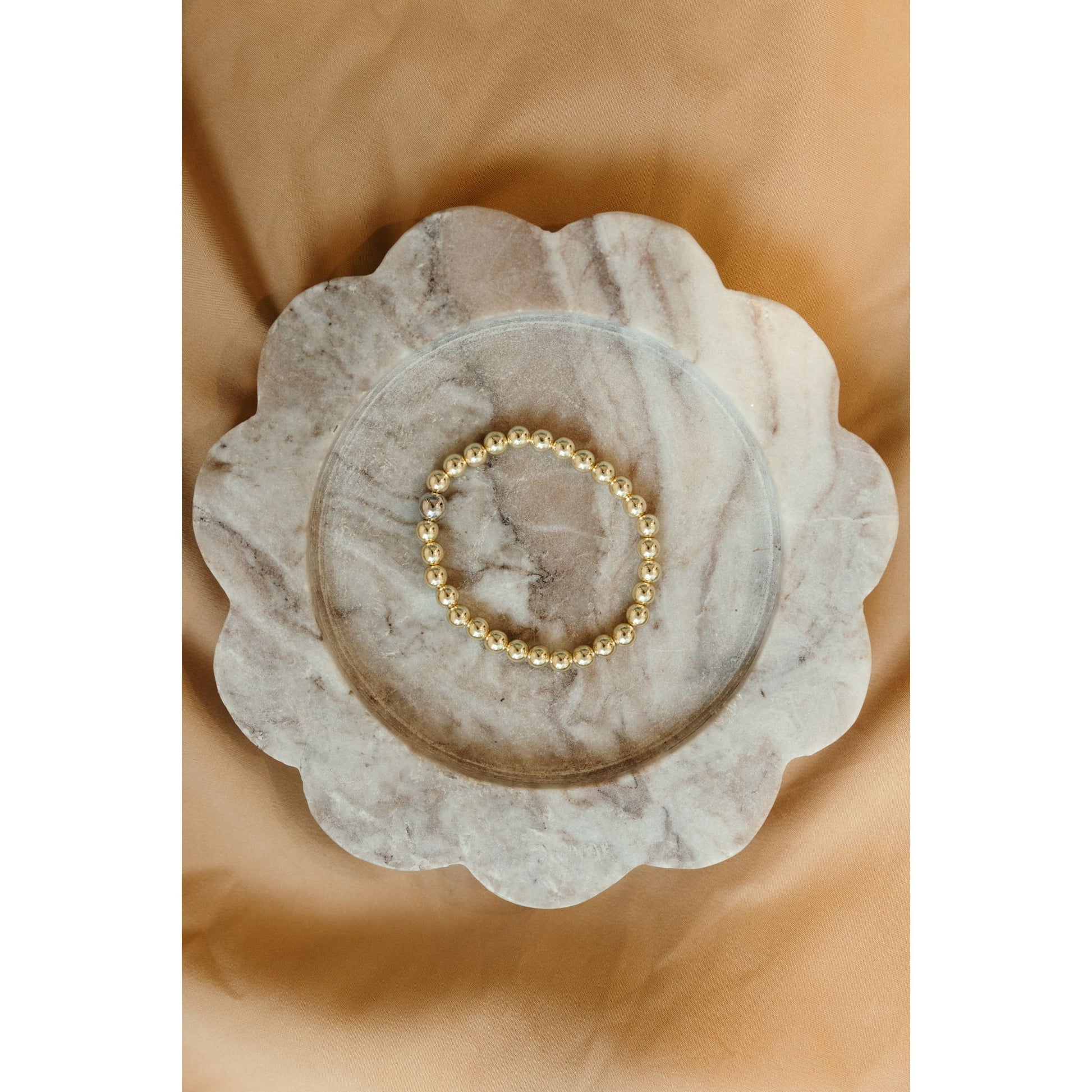Gold beaded bracelet on a marble dish with a beige background