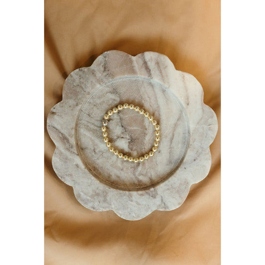 Gold beaded bracelet on a marble dish with a beige background