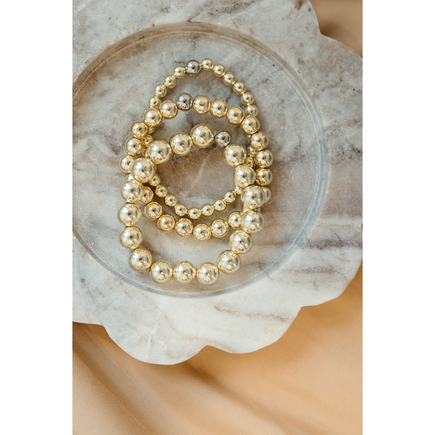 Gold beaded bracelets on a decorative stone surface