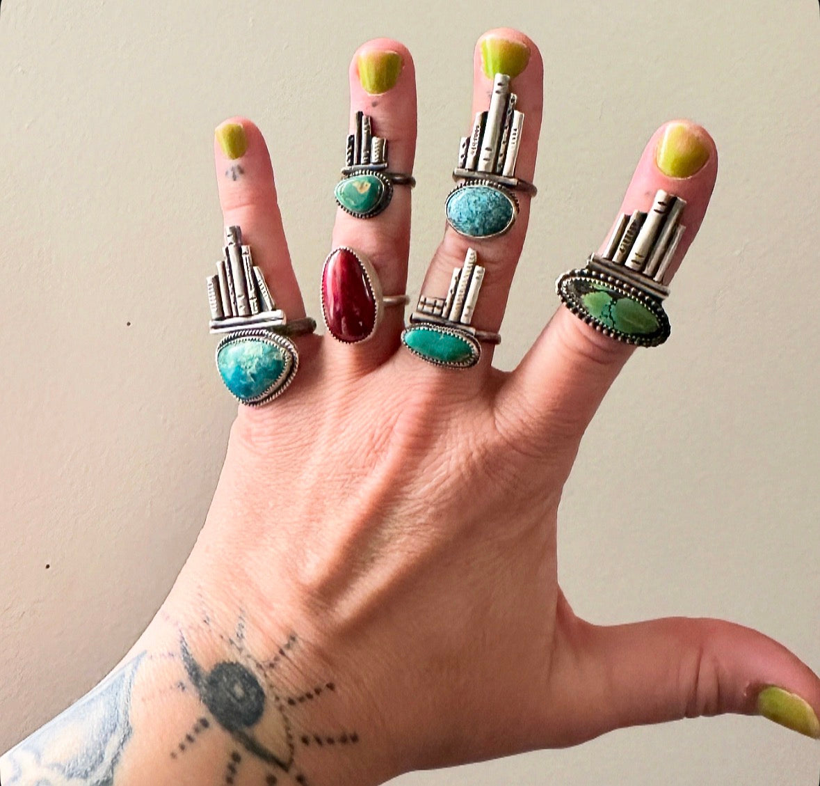Hand wearing multiple rings with turquoise stones and silver bands on a plain background