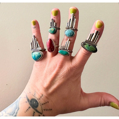 Hand wearing multiple rings with turquoise stones and silver bands on a plain background