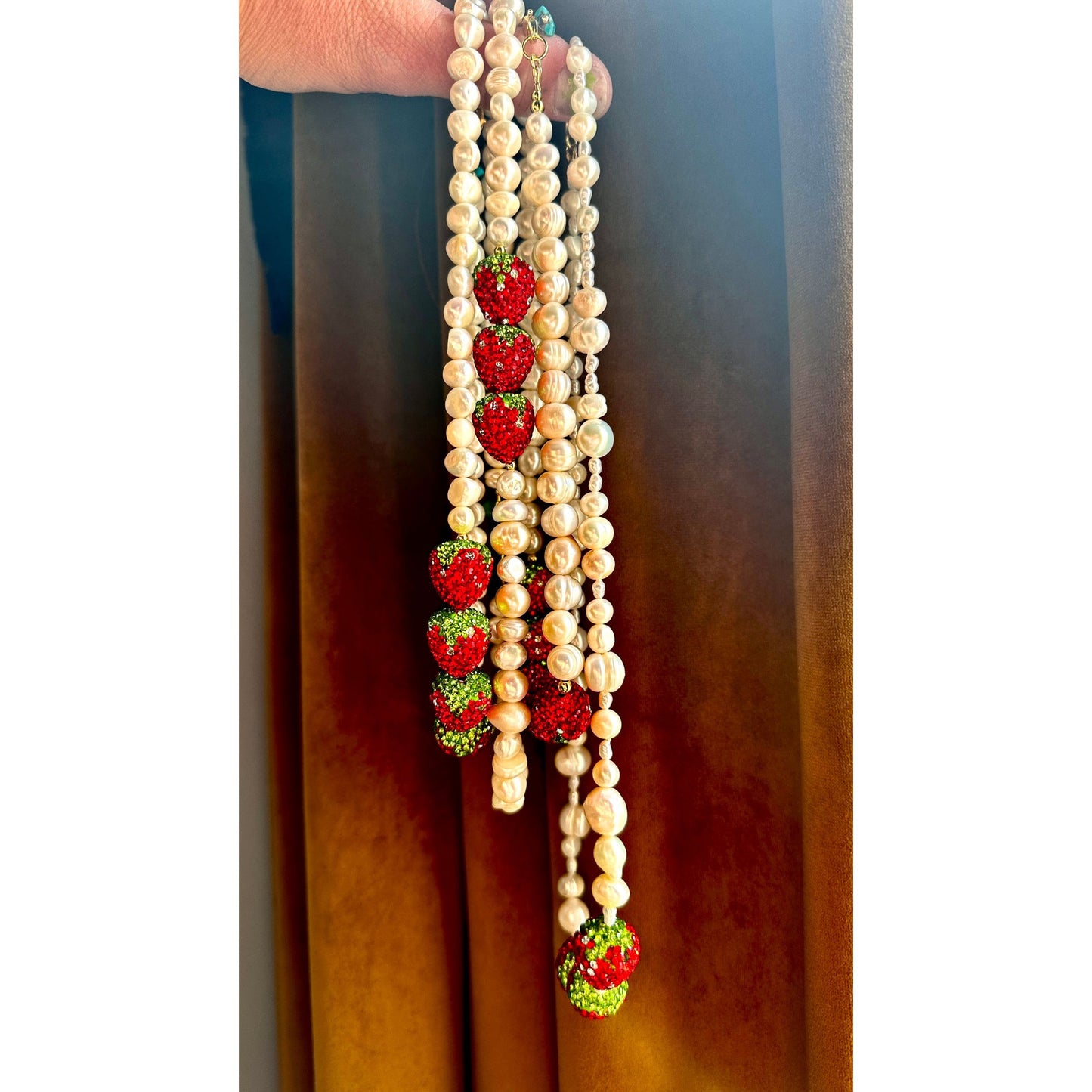 Pearl necklace with strawberry-shaped pendants against a dark background