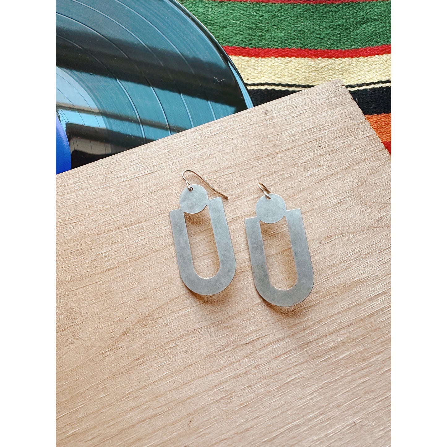 Silver dangle earrings on a wooden surface with a colorful cloth in the background