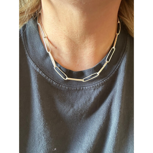 Close-up of a person wearing a silver chain necklace with a dark shirt.