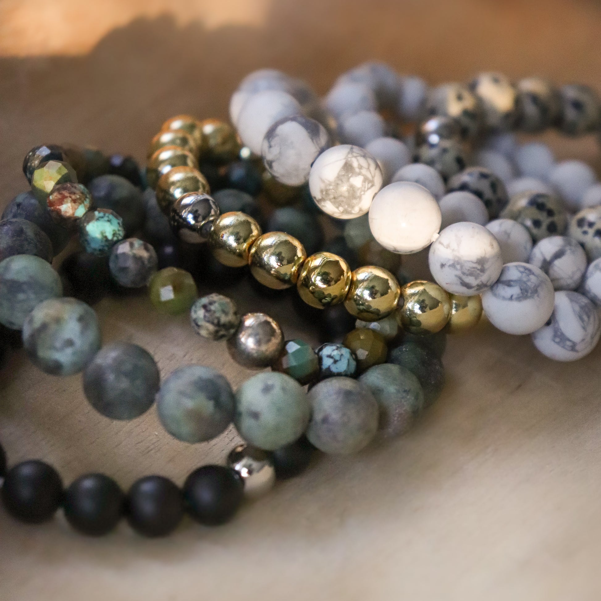 Stack of mixed gemstone bracelets laying on wood surface.