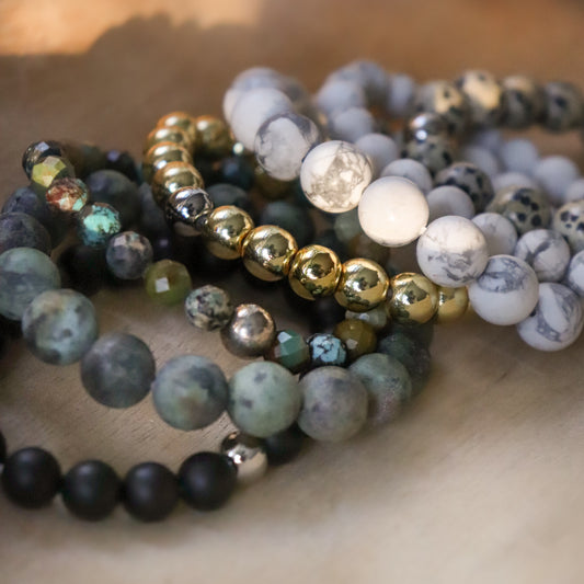 Stack of mixed gemstone bracelets laying on wood surface.