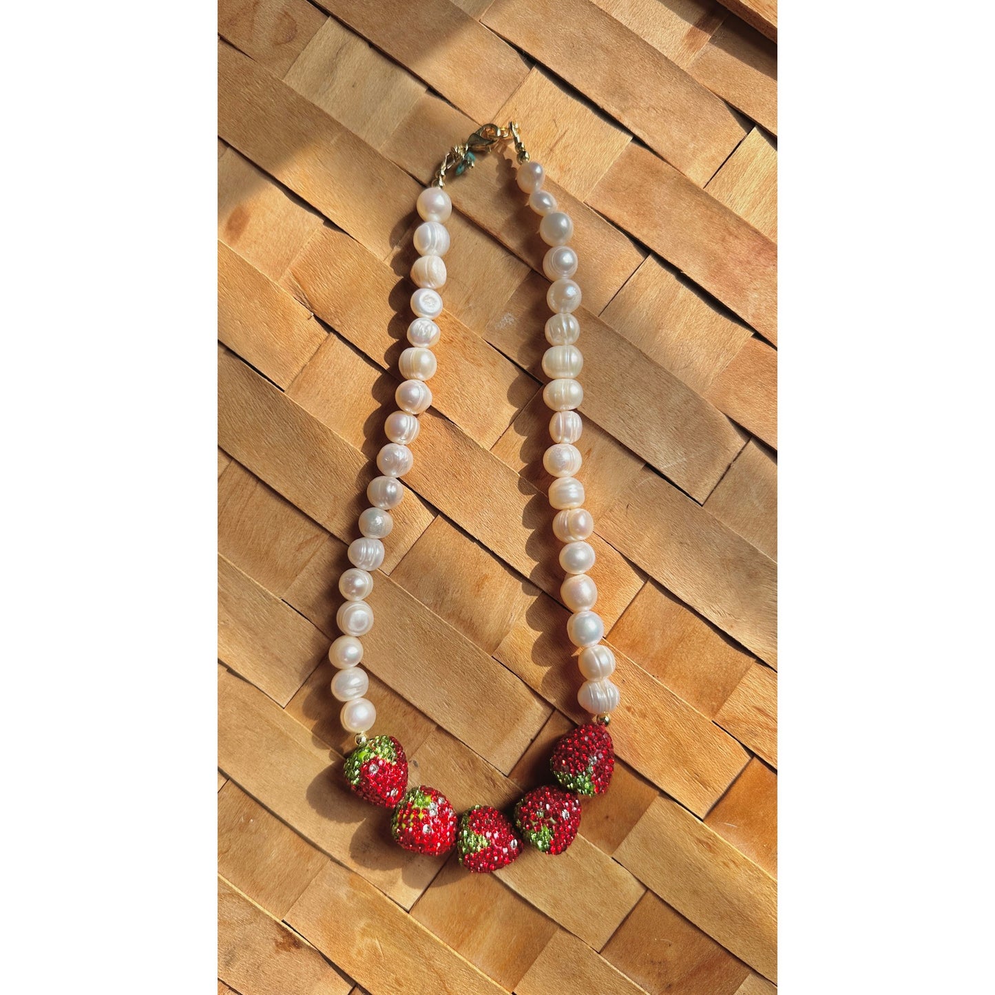 Pearl necklace with strawberry-shaped charms on a wooden surface