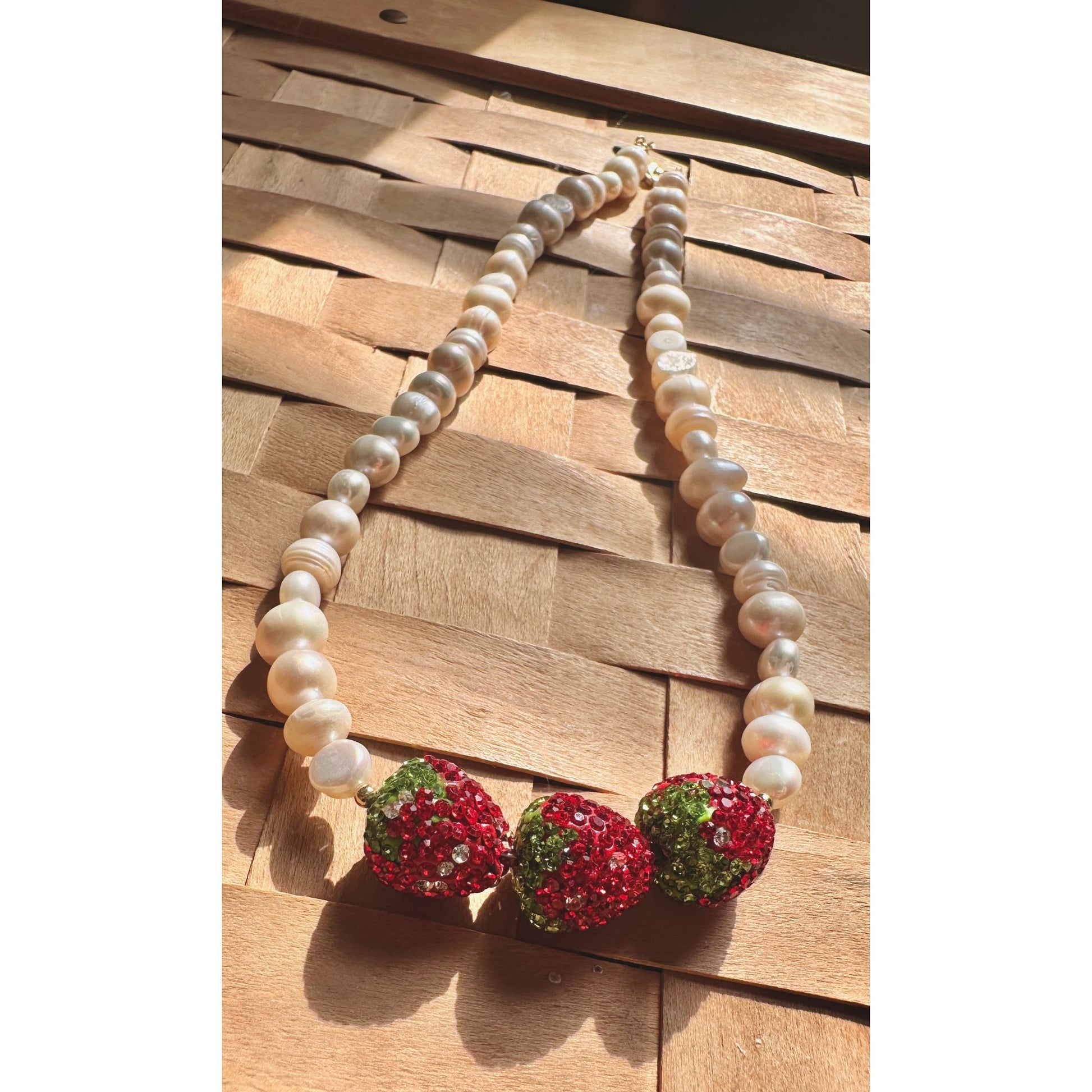 Pearl necklace with red and green beaded pendants on a wooden surface