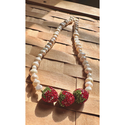 Pearl necklace with red and green beaded pendants on a wooden surface