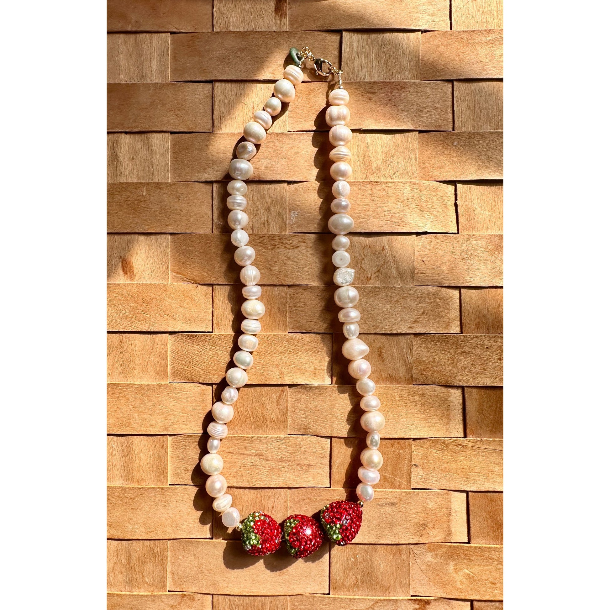 Pearl necklace with red and green accents on a wooden background