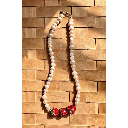 Pearl necklace with red and green accents on a wooden background