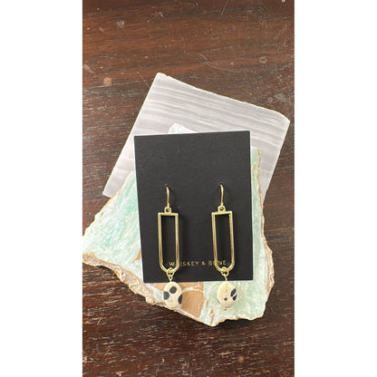 Gold earrings on a black card with 'Whiskey & Bone" branding, placed on a textured surface.