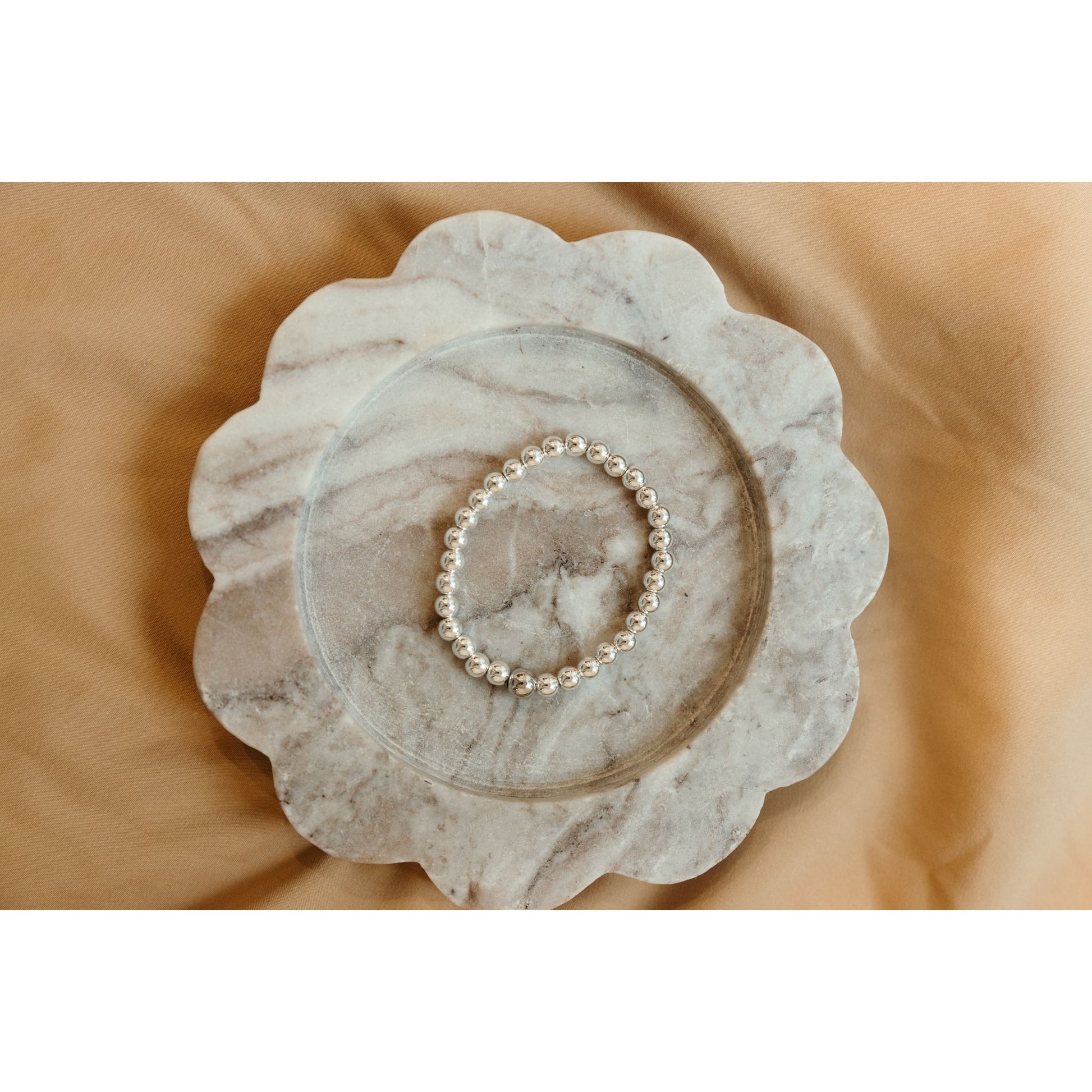 Silver bracelet on a marble dish with a beige background
