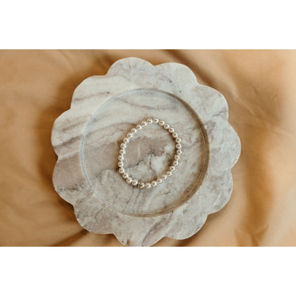 Silver bracelet on a marble dish with a beige background