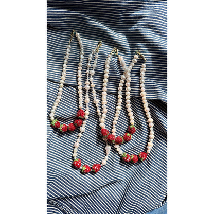 Four pearl necklaces with strawberry decorations on a striped fabric background
