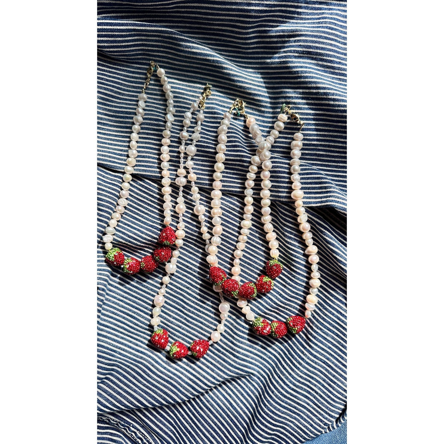 Four pearl necklaces with strawberry decorations on a striped fabric background