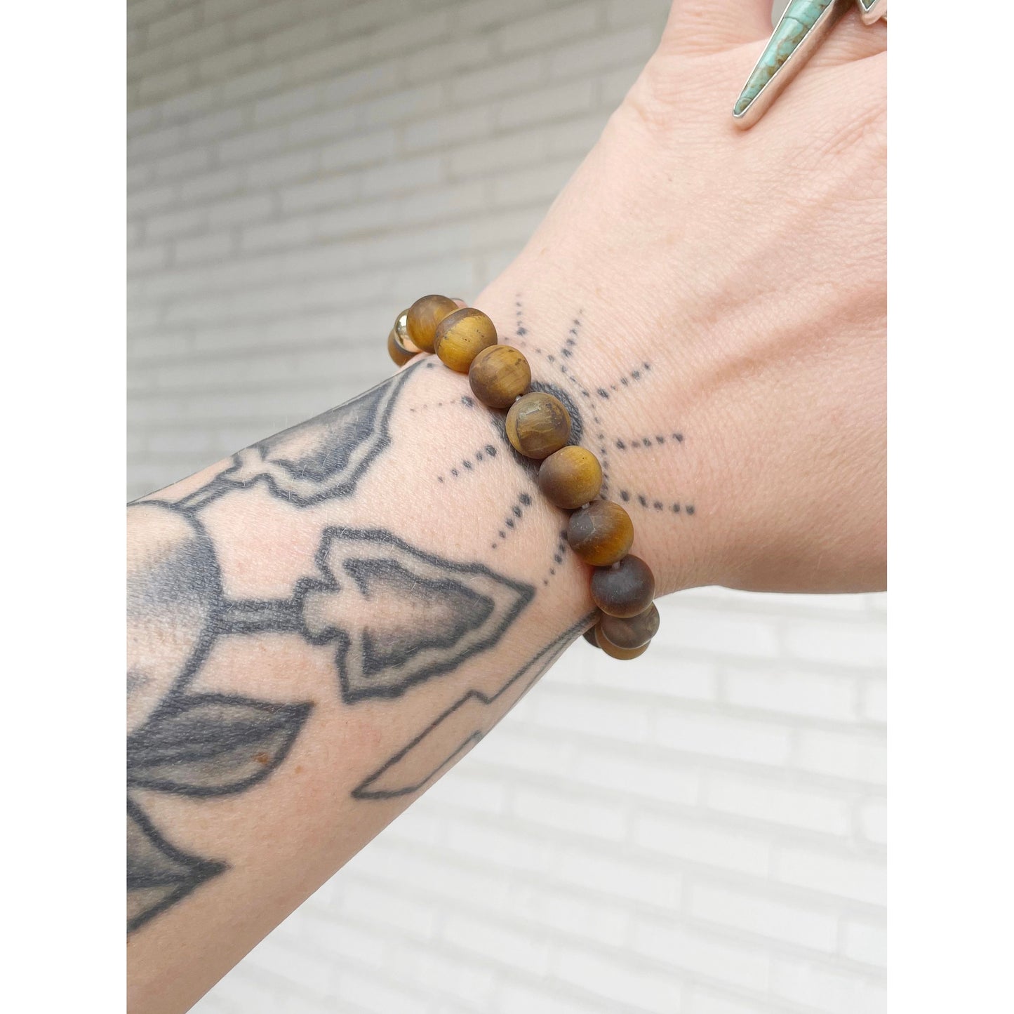 Brown beaded bracelet on a wrist with tattoos against a white background