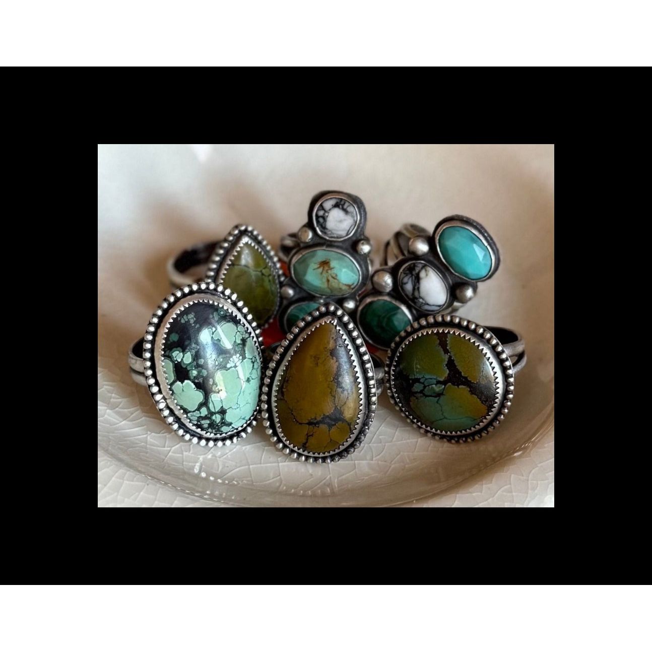 Set of silver rings with turquoise and green gemstones on a textured white surface