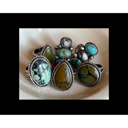 Set of silver rings with turquoise and green gemstones on a textured white surface