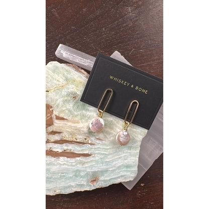 Pair of pearl earrings on a stone surface with 'Whiskey & Bone' packaging.