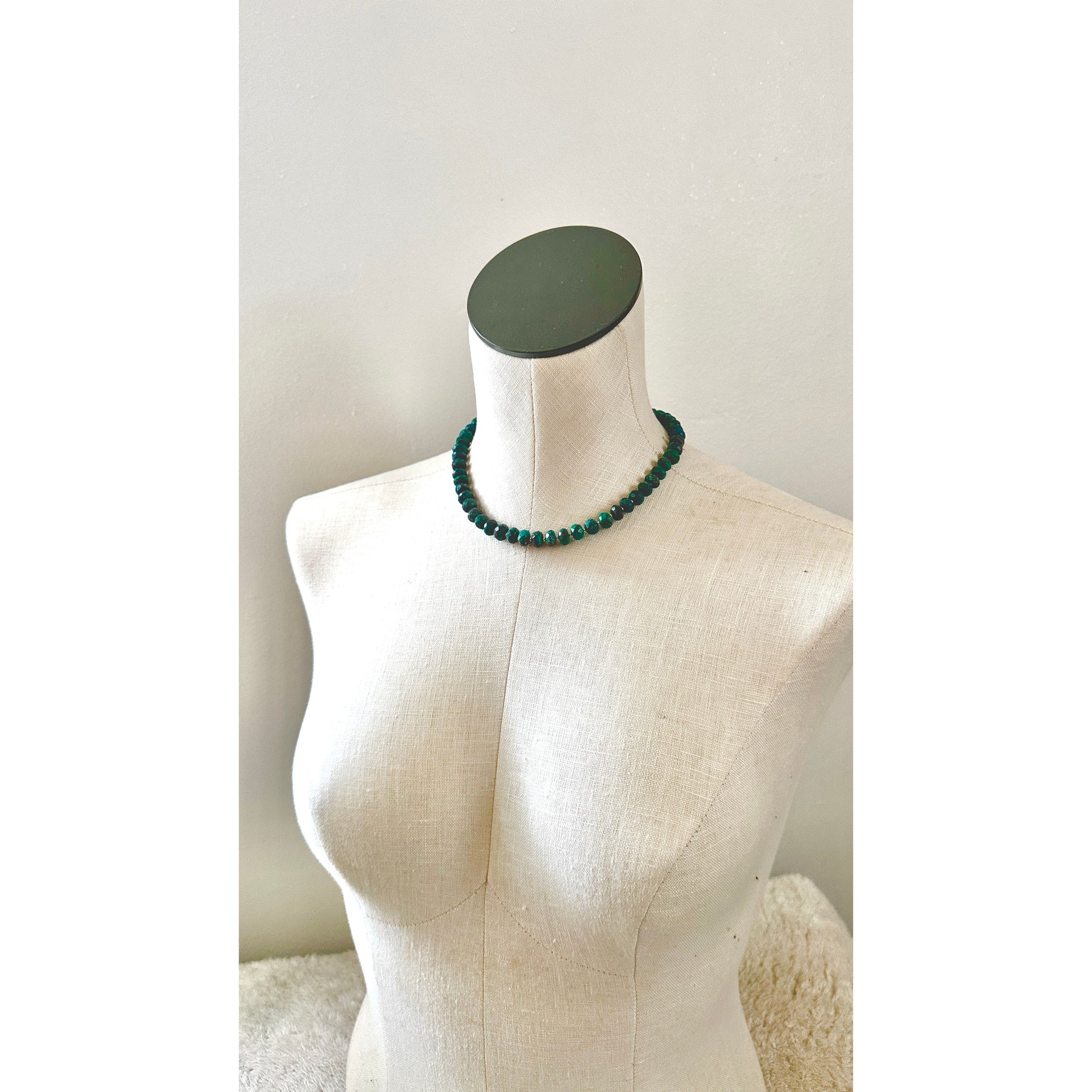 Green beaded necklace on a mannequin bust against a plain background
