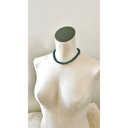 Green beaded necklace on a mannequin bust against a plain background