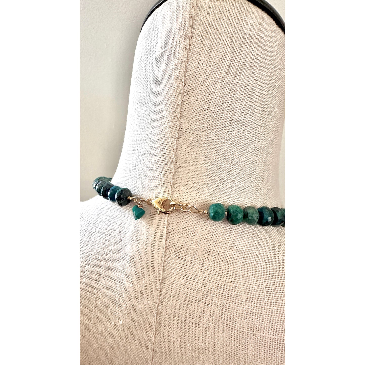 Bracelet with green beads on a mannequin arm against a neutral background