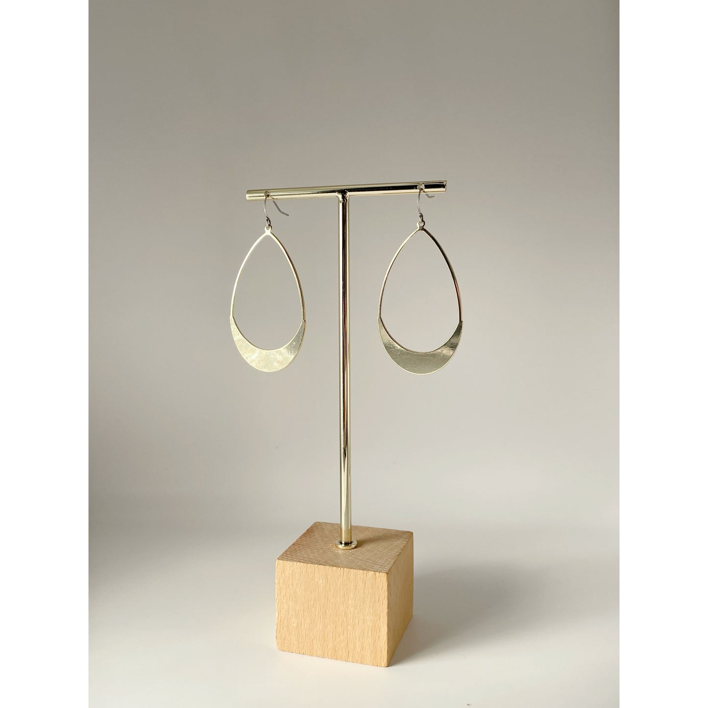 Gold hoop earrings on a wooden stand against a neutral background
