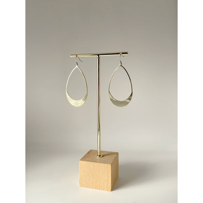 Gold hoop earrings on a wooden stand against a neutral background